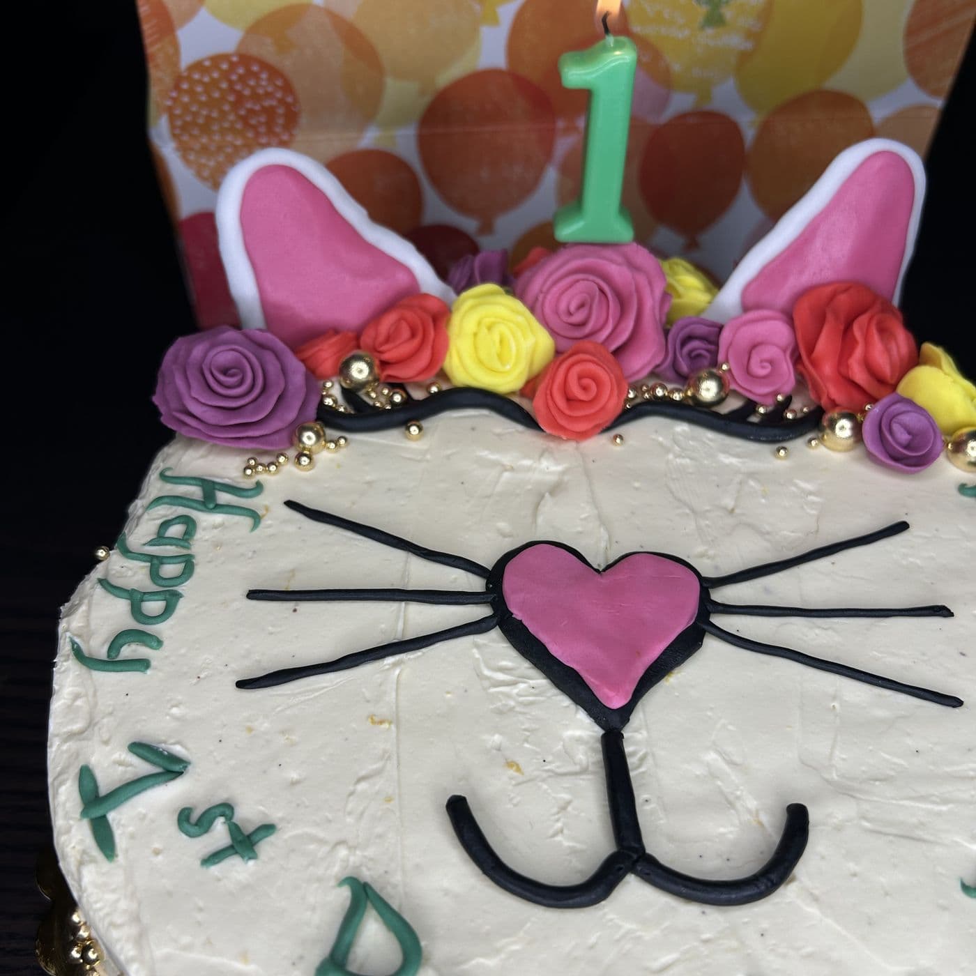 First birthday cake decorated as a cat's face in buttercream, with a crown of pink, purple and yellow sugar roses and fondant ears