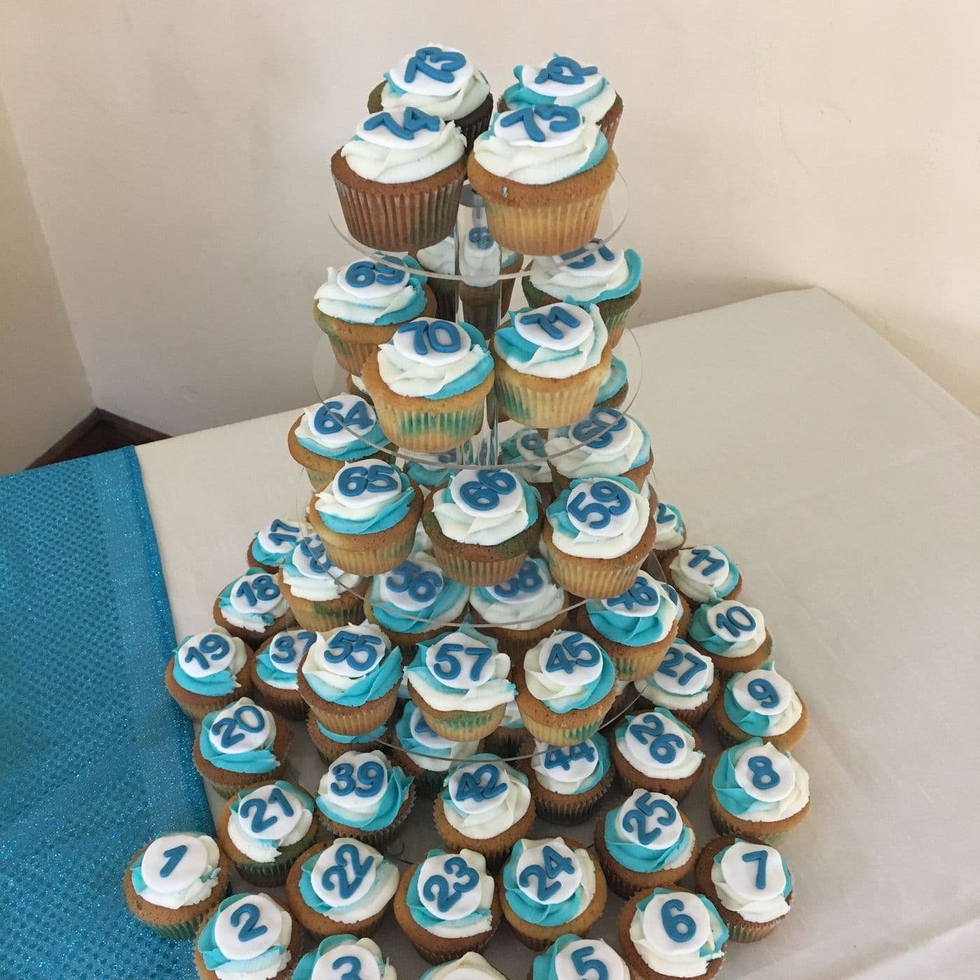A tiered stand of decorated cupcakes iced in blue and white for a celebration