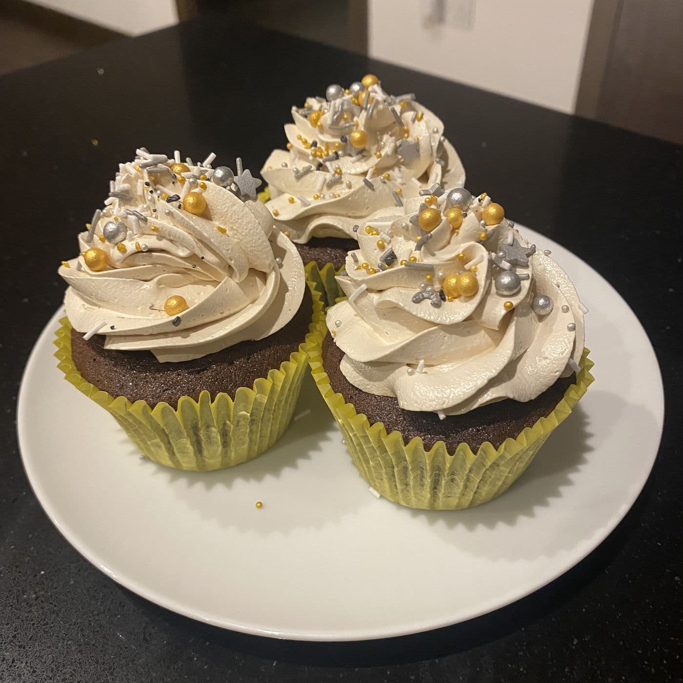 Chocolate cupcakes on a plate, topped with piped buttercream and gold and silver sprinkles