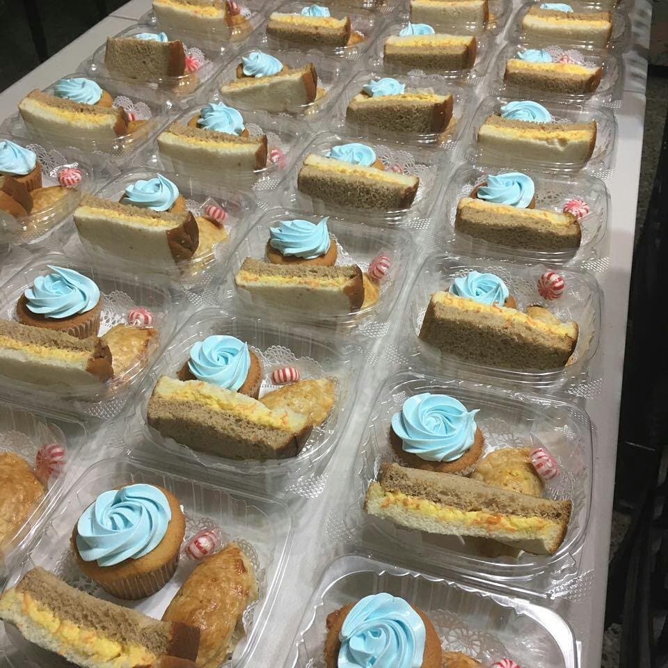 Plates of sandwiches and cupcakes with blue buttercream lined up for a catering order