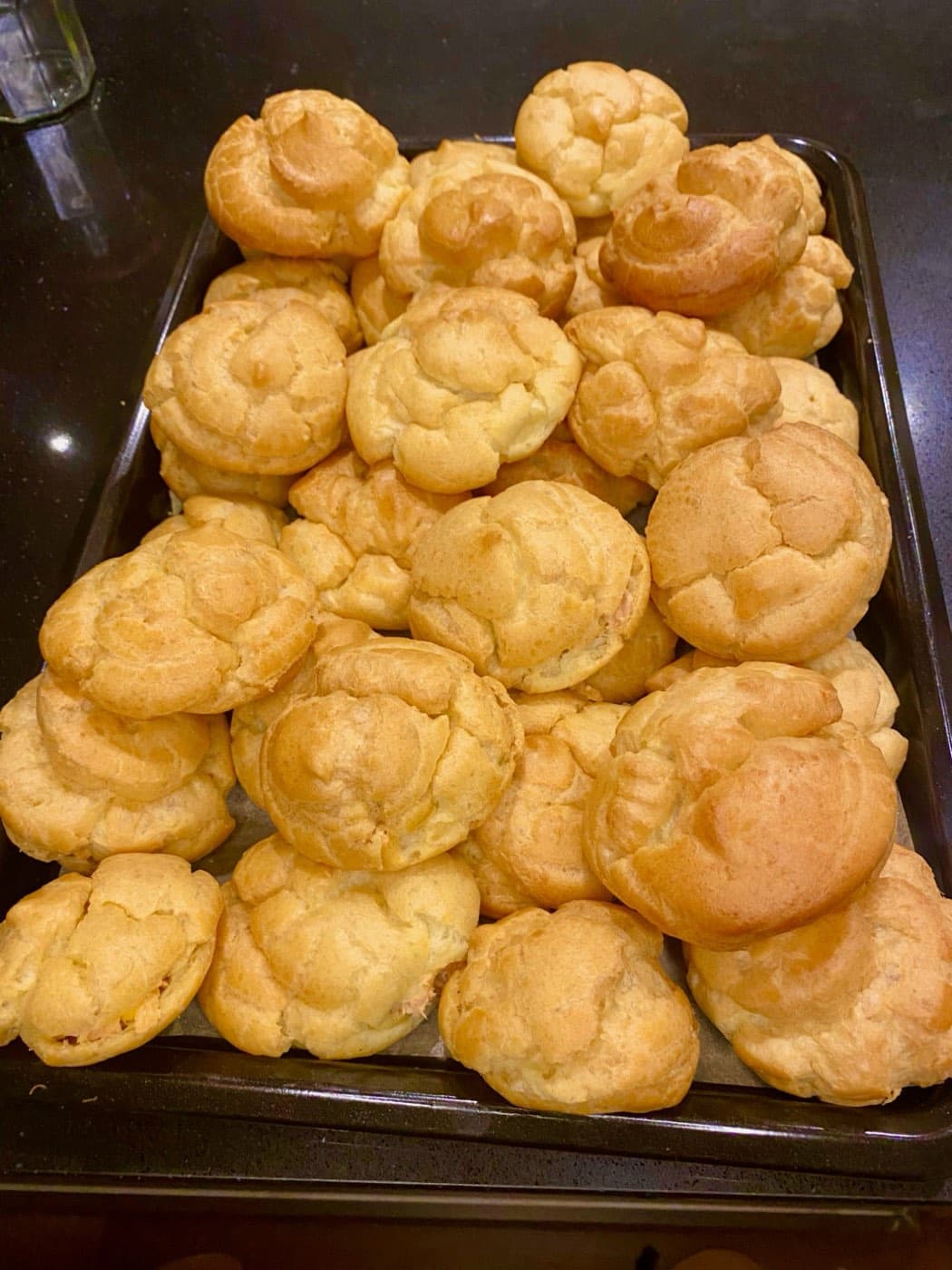 A full tray of golden choux puffs, piped and baked in small batches