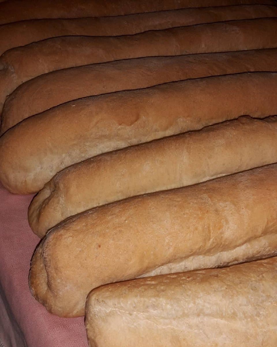 A row of long, soft bread loaves with pale golden crusts, lined up side by side on a cloth
