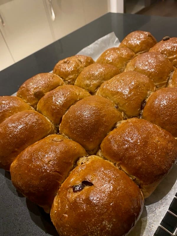 A full batch of glazed buns on parchment, fresh out of the oven