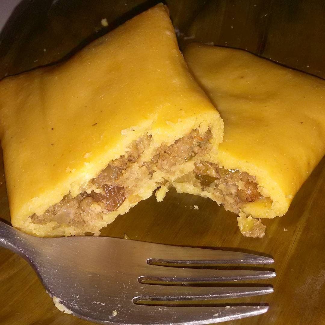 A cornmeal pastelle broken open on its banana leaf, the seasoned minced meat filling showing