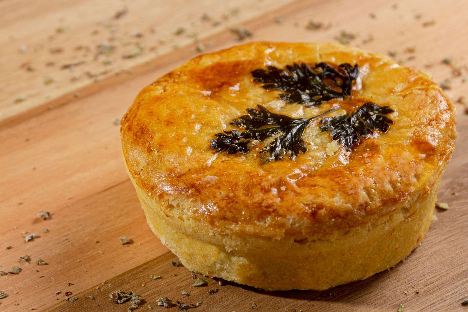 A deep golden pie glazed and finished with pastry herbs, resting on a wooden board
