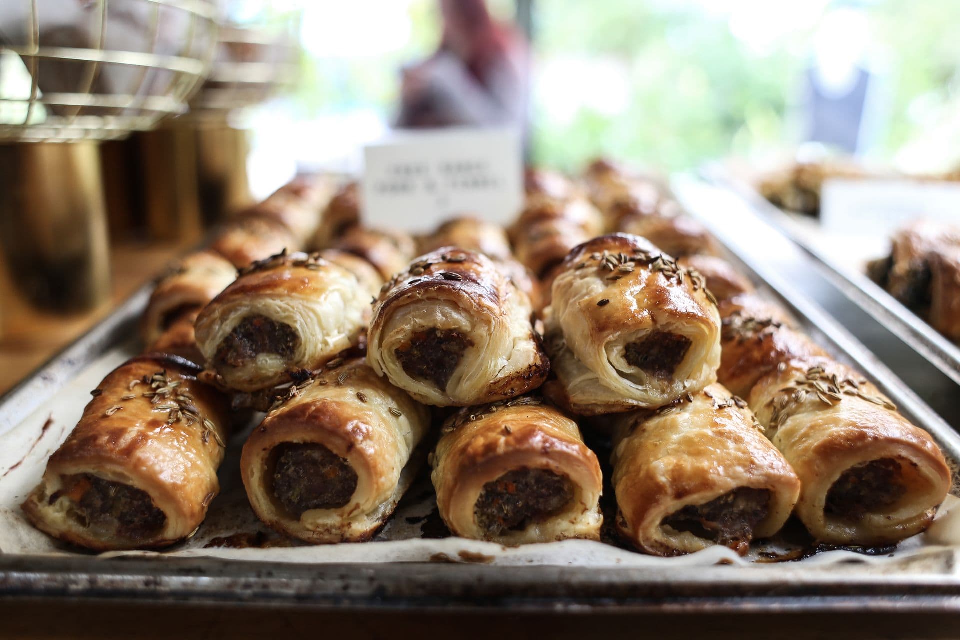 A tray of golden sausage rolls stacked on a bakery counter