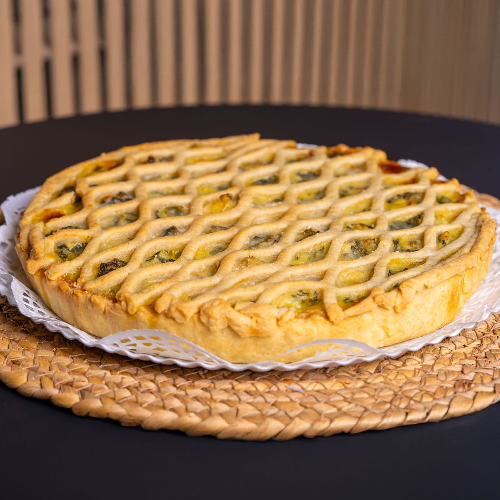 A lattice-topped vegetable pie on a dark table, the filling showing through the pastry