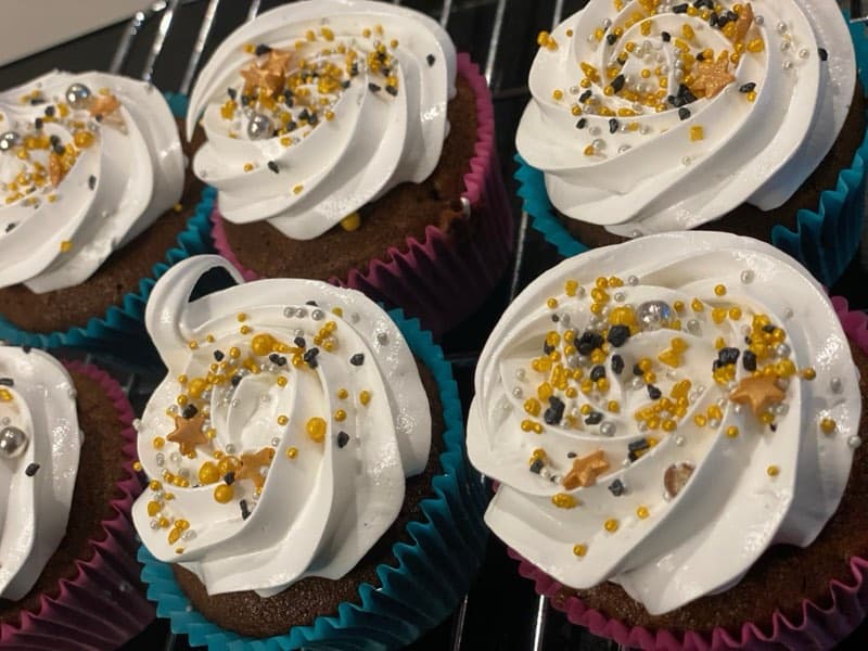Cupcakes with tall white buttercream swirls and gold sprinkles on a cooling rack