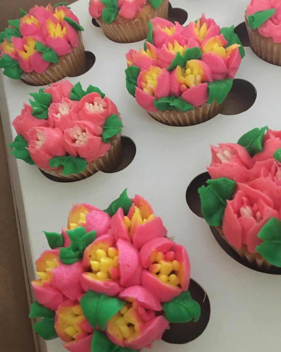 Cupcakes piped with pink and yellow buttercream flowers and green leaves, sitting in a white cupcake box insert