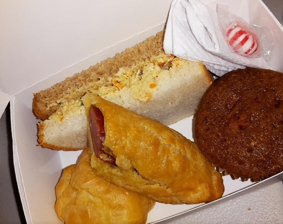 A lunch box with a sandwich on white and brown bread, a sausage in pastry, a choux puff and a plain cupcake