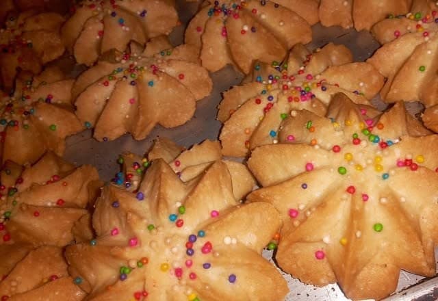 Piped rosette butter cookies topped with hundreds and thousands on a baking tray