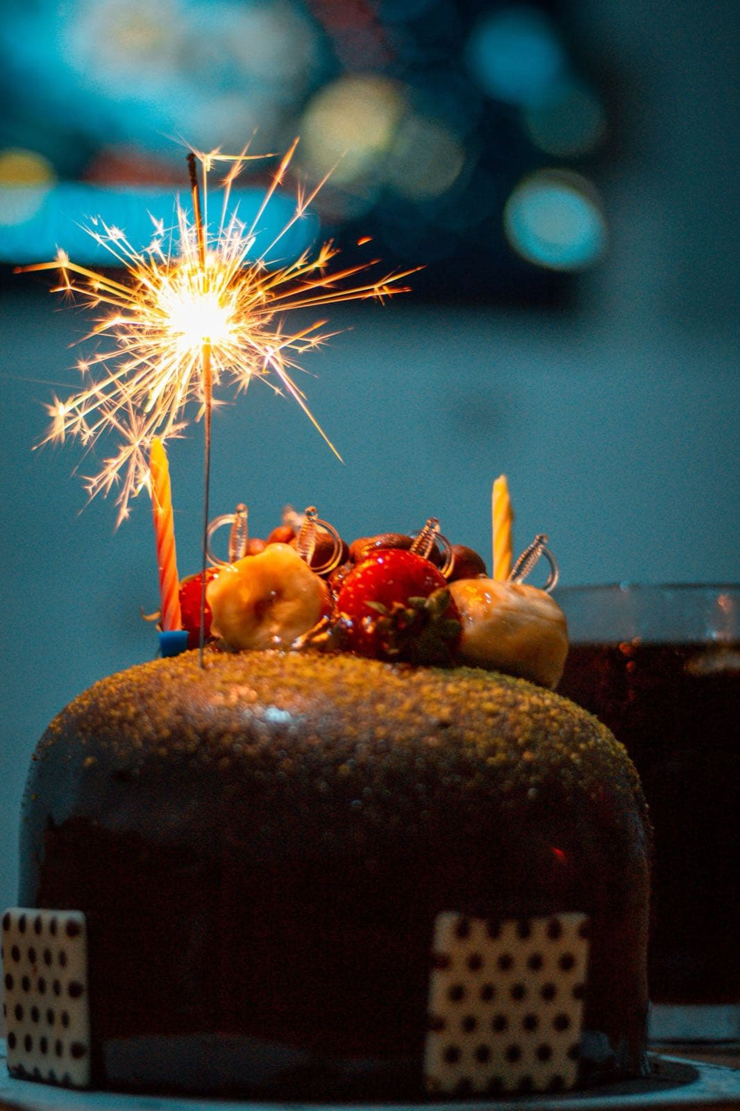 A celebration cake lit by a sparkler in a dark room