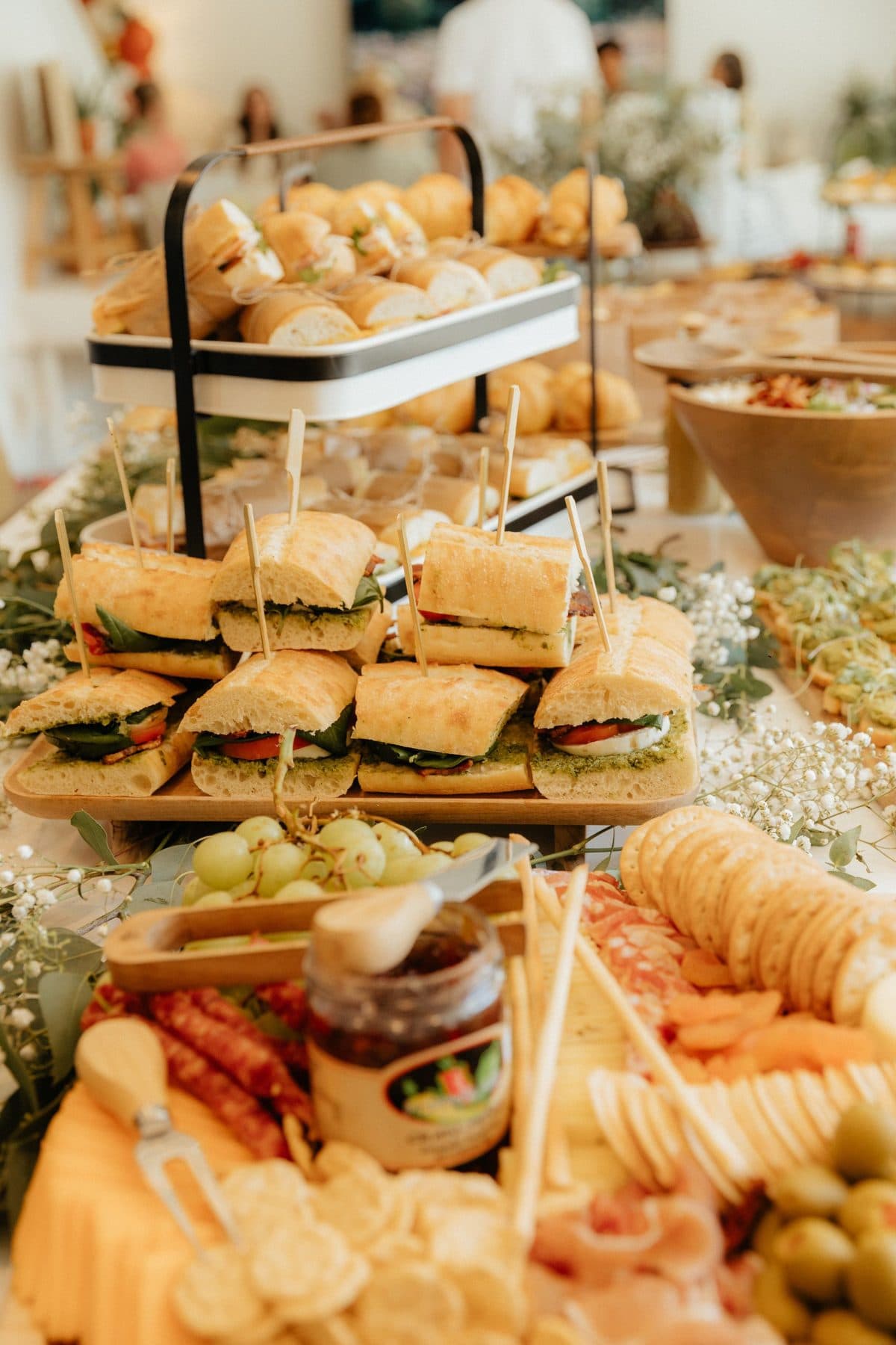A party buffet table with tiered sandwiches, cheese, crackers and savoury bites