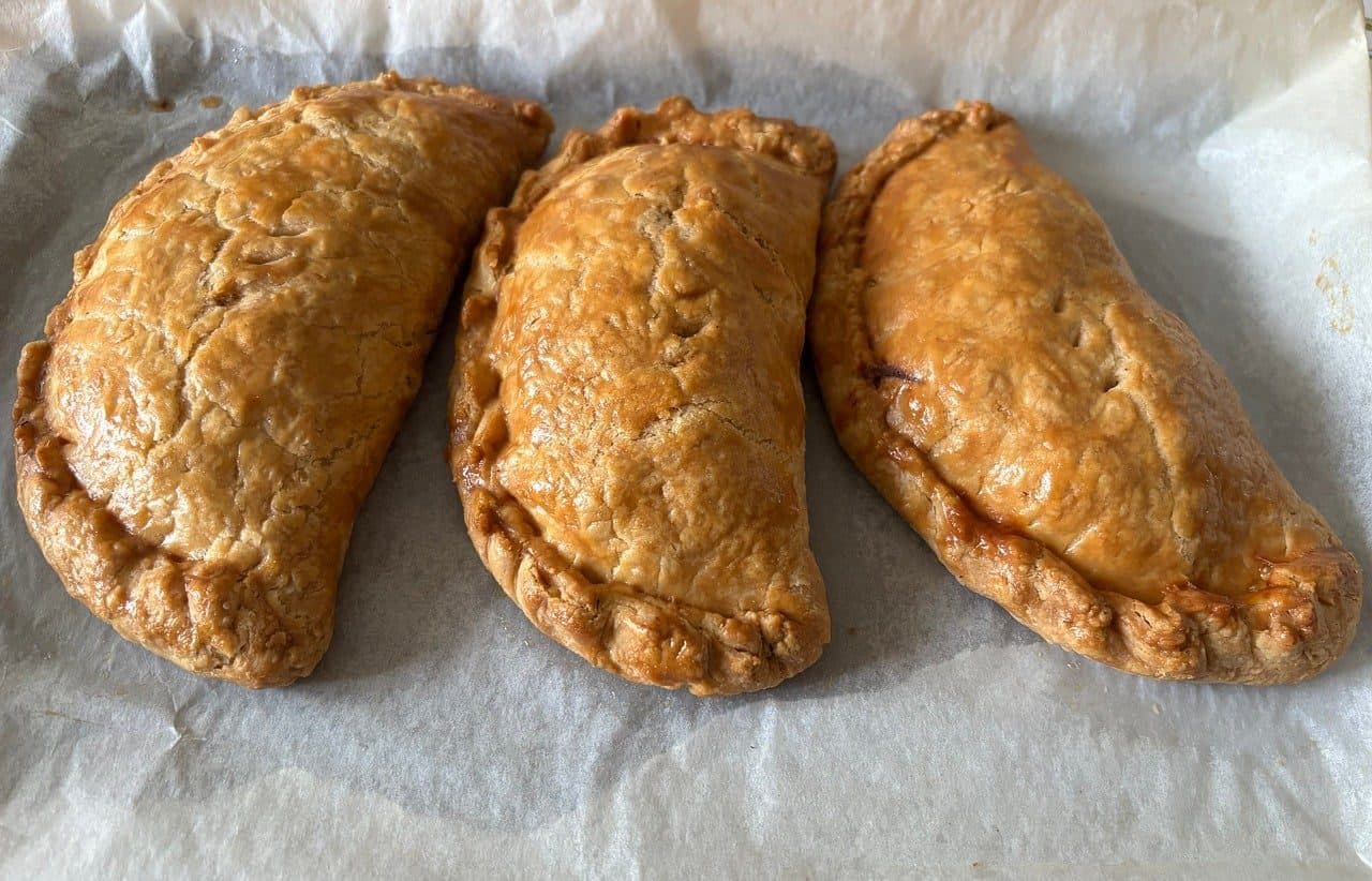 Three golden, glazed half-moon pies with hand-crimped edges on baking paper