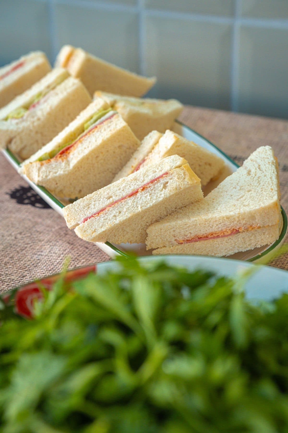 Rows of triangle sandwiches on a platter beside a green salad