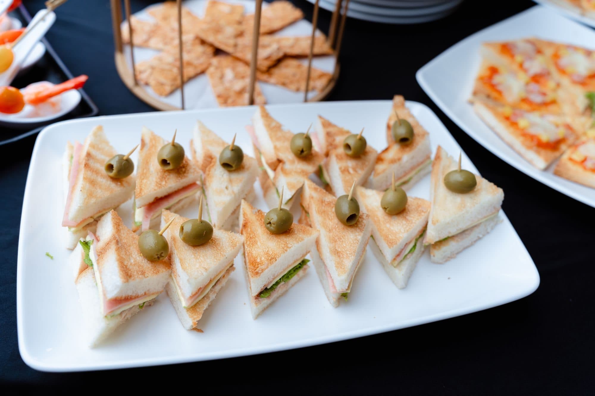 Toasted triangle sandwiches topped with olives on a white platter