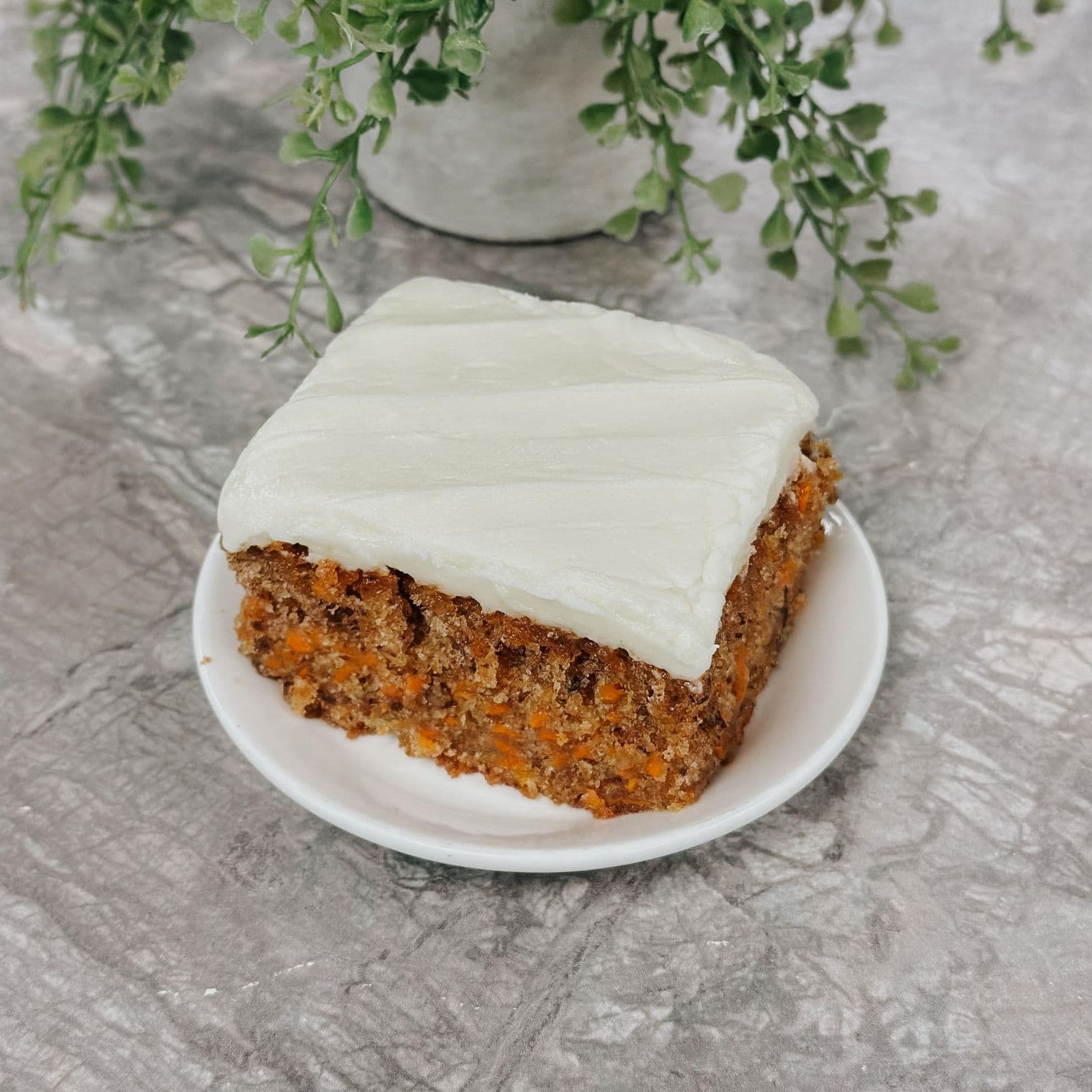 A thick slice of spiced carrot cake under a smooth layer of pale icing
